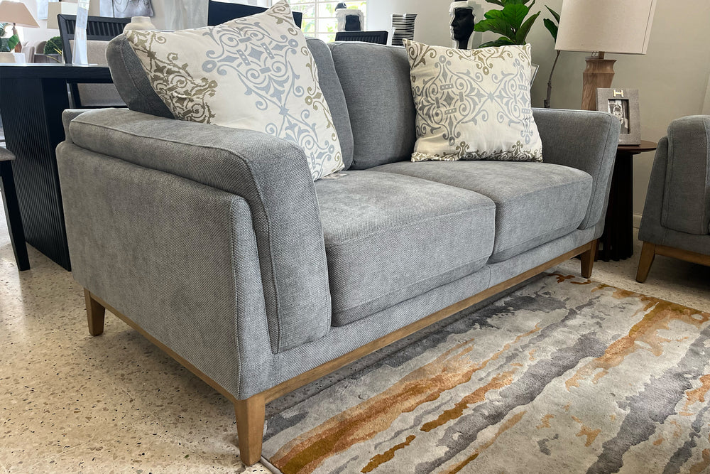 Loveseat gris con patas de madera sobre fondo blanco.