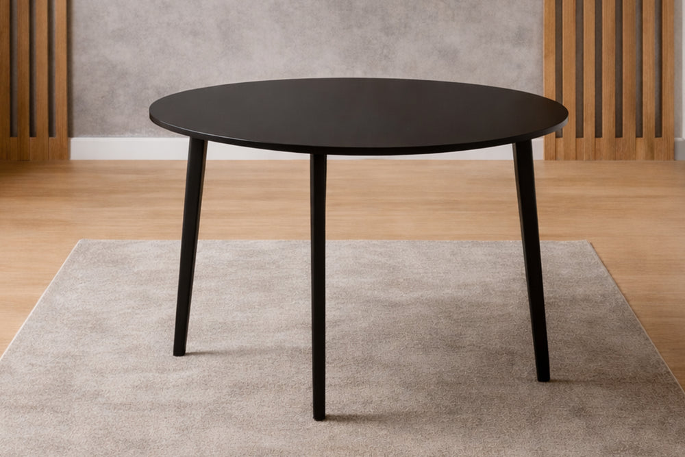 Mesa de comedor redonda negra con patas cónicas sobre una alfombra beige, piso de madera clara, estilo escandinavo minimalista.