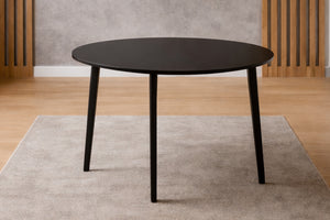 Mesa de comedor redonda negra con patas cónicas sobre una alfombra beige, piso de madera clara, estilo escandinavo minimalista.