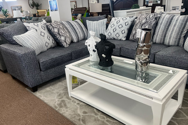 Seccional gris con cojines estampados y una mesa de centro blanca en madera en una sala de exposición