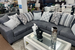 Seccional gris con cojines estampados en un entorno de tienda de muebles.