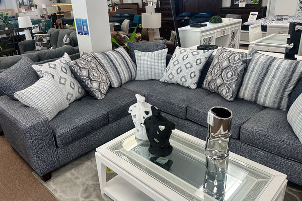 Seccional gris con cojines estampados en un entorno de tienda de muebles.