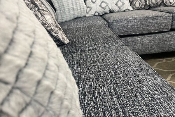 Sofá seccional gris texturizado con cojines estampados.