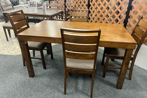 Juego de comedor con mesa rectangular de madera en tono nogal y cuatro sillas a juego con respaldos de listones horizontales y asientos tapizados en gris. Exhibido en tienda de muebles, destaca su diseño funcional y estilo contemporáneo.