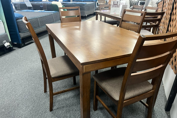Mesa de comedor rectangular de madera en tono cálido con cuatro sillas a juego, respaldos de listones horizontales y asientos tapizados en gris. Conjunto de estilo contemporáneo exhibido en una tienda de muebles.