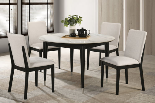 Mesa de comedor redonda puesta con cuatro sillas en una habitación con grandes ventanas.