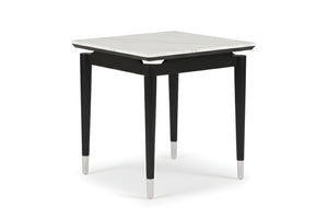 Una mesa de esquina con tope cuadrado de imitación de mármol blanco y patas negras y cónicas, cada una rematada con una virola de plata o cromo. La mesa está colocada sobre un fondo blanco. 