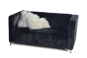 Loveseat negro acanalado con una manta de piel blanca sobre un fondo blanco.