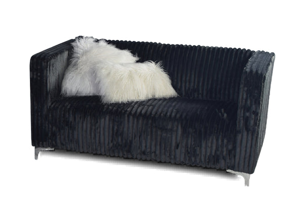 Loveseat negro acanalado con una manta de piel blanca sobre un fondo blanco.