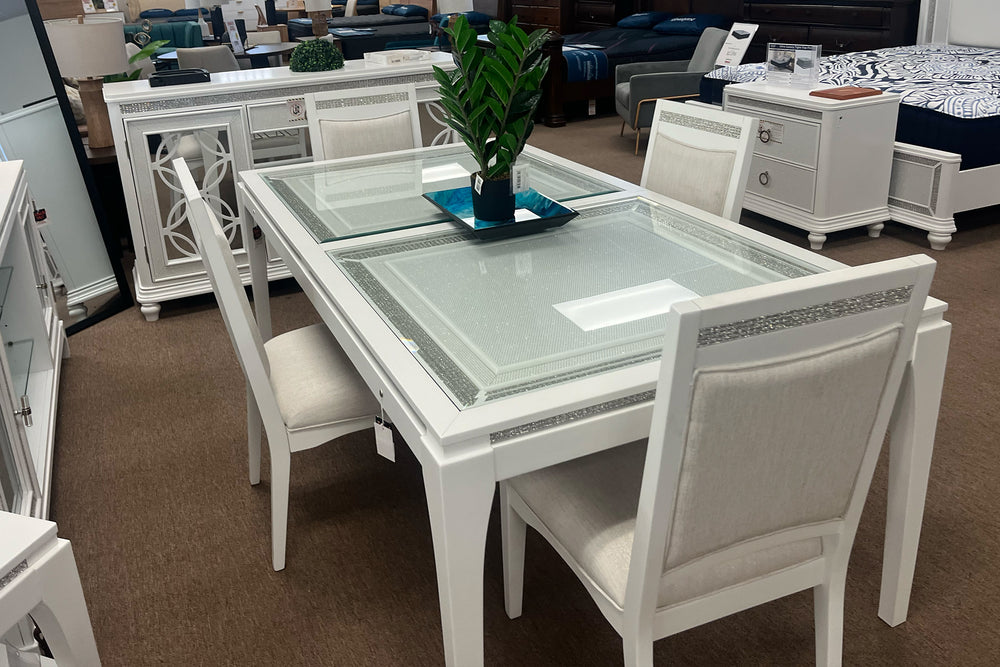 Mesa blanca con cuatro sillas con acolchado crema en un sala de comedor con objetos decorativos. 