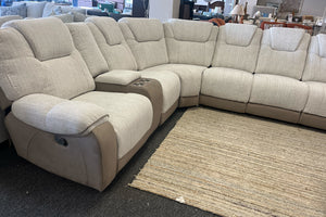 Sofá modular beige con asientos reclinables sobre un suelo alfombrado en una sala de exposición 