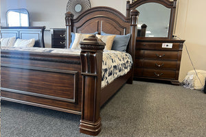 Cama de madera marrón oscura con acolchado colorido y un gavetero con espejo en el fondo. 