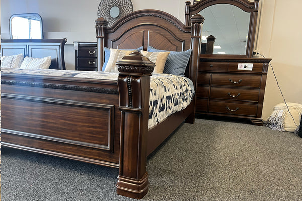 Cama de madera marrón oscura con acolchado colorido y un gavetero con espejo en el fondo. 