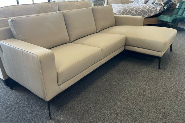 Sofá seccional beige sobre una alfombra gris. En un entorno de exposición