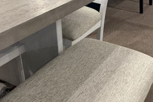 Primer plano de sillas de comedor con asientos tapizados en tela beige texturizada junto a una mesa de acabado madera en tonos gris claro. La combinación de superficies suaves y vetas visibles aporta un estilo rústico moderno y acogedor.