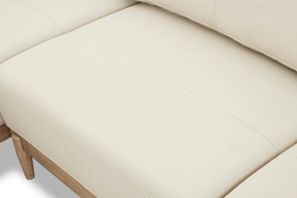 Primer plano de un sofá chaise beige con patas de madera sobre un fondo claro.