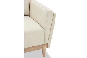 Esquina de sofá chaise beige con patas de madera y con costura visible sobre fondo blanco.