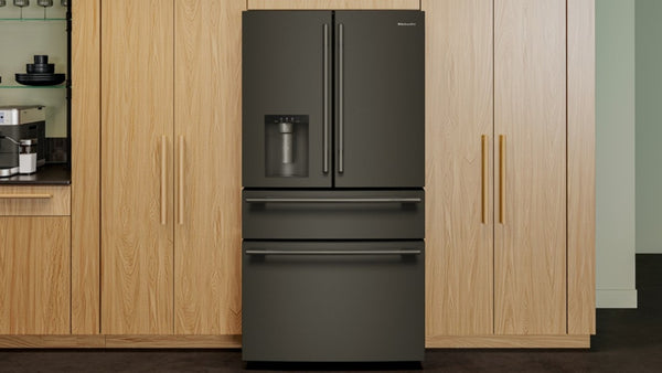Una nevera estilo puerta francesa de color gris oscuro con un cajón congelador inferior, ubicada entre gabinetes de cocina de madera clara.