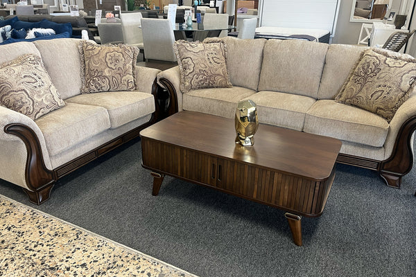 Loveseat sofá marrón con cojines estampados y una mesa de centro de madera en un ambiente de sala de exposición.