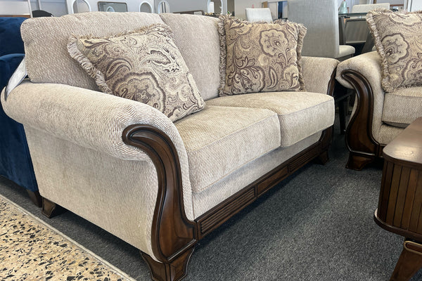 Loveseat con cojines estampados y una mesa de centro de madera en un ambiente de sala de exposición.