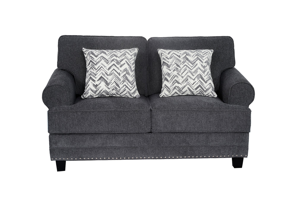 Loveseat tapizado en tela gris oscuro con brazos redondeados, cojines decorativos con patrón en zigzag gris y blanco, detalles de tachuelas metálicas en la base y patas negras de madera.