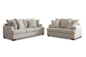 Juego de sala compuesto por sofá y loveseat tapizados en tela color beige claro, con cojines decorativos a juego y patas de madera oscura. Presentado sobre fondo blanco para resaltar el diseño contemporáneo y las líneas limpias del conjunto.