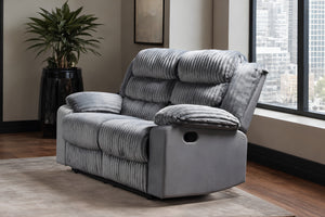 Love seat reclinable de pana gris con cojines decorativos a juego, en un salón moderno con ventana, vista a la ciudad y una planta en maceta.