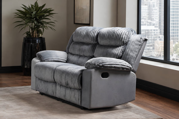 Love seat reclinable de pana gris con cojines decorativos a juego, en un salón moderno con ventana, vista a la ciudad y una planta en maceta.