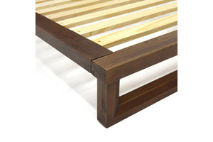 Primer plano de una esquina de la estructura de madera de la cama con listones sobre fondo blanco.