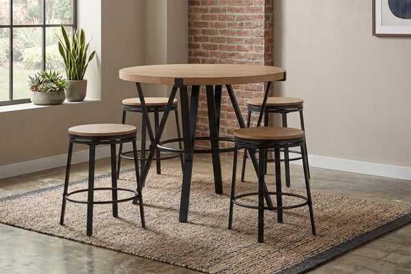 Juego de comedor tipo pub con mesa redonda de altura de mostrador y cuatro taburetes a juego. Diseño industrial con estructura metálica negra y superficie de madera clara, ubicado sobre una alfombra en un espacio de estilo urbano y acogedor.