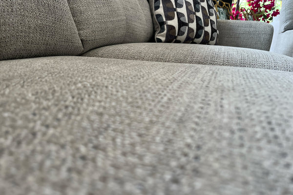 Sofá beige con tela texturizada y cojines decorativos en una sala de exposición