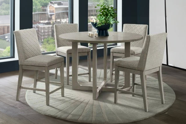 Juego de comedor contemporáneo con mesa redonda de acabado gris claro y cuatro sillas tapizadas en tela color crema con respaldo acolchado. El conjunto se encuentra sobre una alfombra redonda a juego frente a amplios ventanales que aportan luz natural.