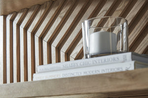 Pila de libros sobre una estantería de madera con un recipiente de vidrio al fondo.