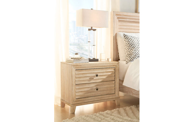 Mesita de noche de madera con lámpara junto a la cama en un dormitorio.