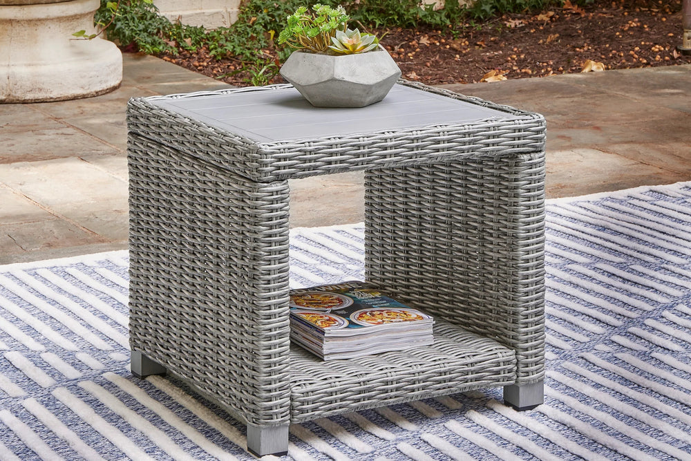 Mesa auxiliar de mimbre gris sobre fondo blanco.