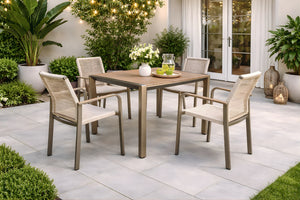 Juego de comedor para exterior con mesa cuadrada y cuatro sillas de estructura metálica en tono beige. Ubicado en un patio moderno con plantas decorativas, iluminación ambiental y superficies de losas en tonos claros.