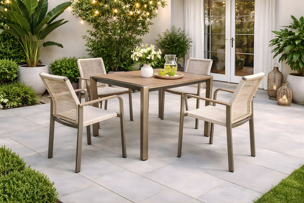 Juego de comedor para exterior con mesa cuadrada y cuatro sillas de estructura metálica en tono beige. Ubicado en un patio moderno con plantas decorativas, iluminación ambiental y superficies de losas en tonos claros.