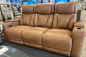Sofá reclinable de tres plazas en color café claro con respaldo acolchado, reposacabezas amplios, controles laterales y portavasos integrados en los reposabrazos, exhibido en una tienda de muebles.