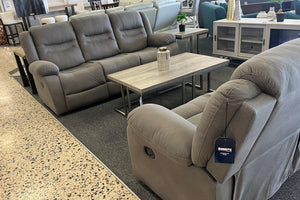 Sala de exhibición con sofá y sillón reclinables en color gris, ambos con asientos acolchados y respaldo acolchado, acompañados de una mesa de centro rectangular con acabado de madera clara.