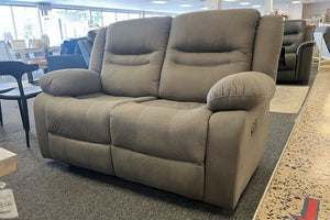 Loveseat reclinable en color gris claro con asientos acolchados, respaldos altos y brazos amplios acolchados, exhibido en una tienda de muebles.