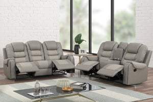 Juego de sala reclinable en color gris claro con sofá de tres plazas y loveseat de dos plazas, ambos con reposapiés extendidos, respaldos acolchados, detalles acolchados en los asientos y consola central con portavasos, ubicado en una sala moderna con mesa de centro de vidrio y ventanas amplias.