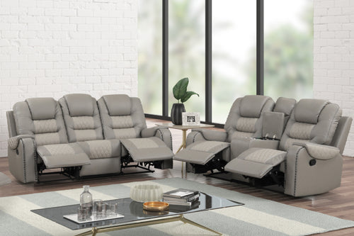 Juego de sala reclinable en color gris claro con sofá de tres plazas y loveseat de dos plazas, ambos con reposapiés extendidos, respaldos acolchados, detalles acolchados en los asientos y consola central con portavasos, ubicado en una sala moderna con mesa de centro de vidrio y ventanas amplias.