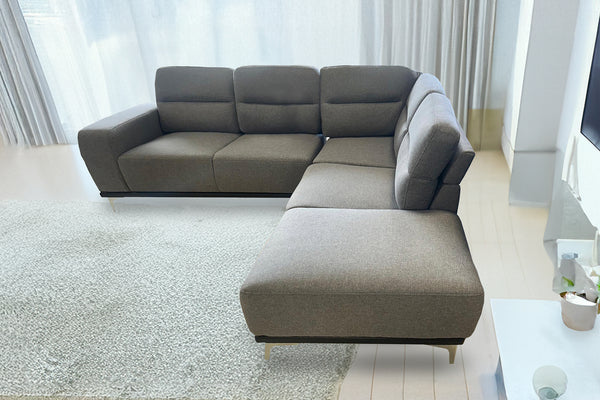 Sofá seccional gris en una sala moderna con paredes y piso de colores claros.