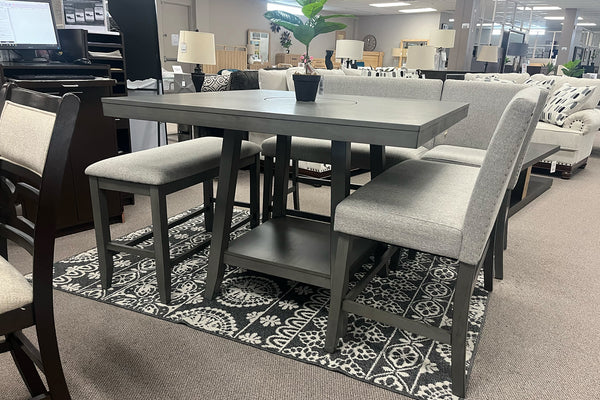 Juego de comedor de altura mostrador con mesa rectangular gris, dos bancos tapizados y sillas a juego en tela gris claro. Incluye repisa inferior para almacenamiento y se presenta en una sala de exhibición con estilo contemporáneo.