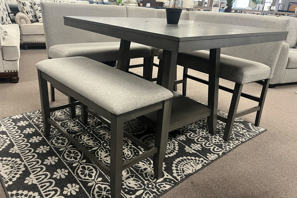 Juego de comedor de altura mostrador con mesa cuadrada en acabado gris oscuro, dos bancos tapizados y asientos con respaldo en tela gris claro. Incluye repisa inferior de almacenamiento y diseño contemporáneo, exhibido sobre una alfombra decorativa.