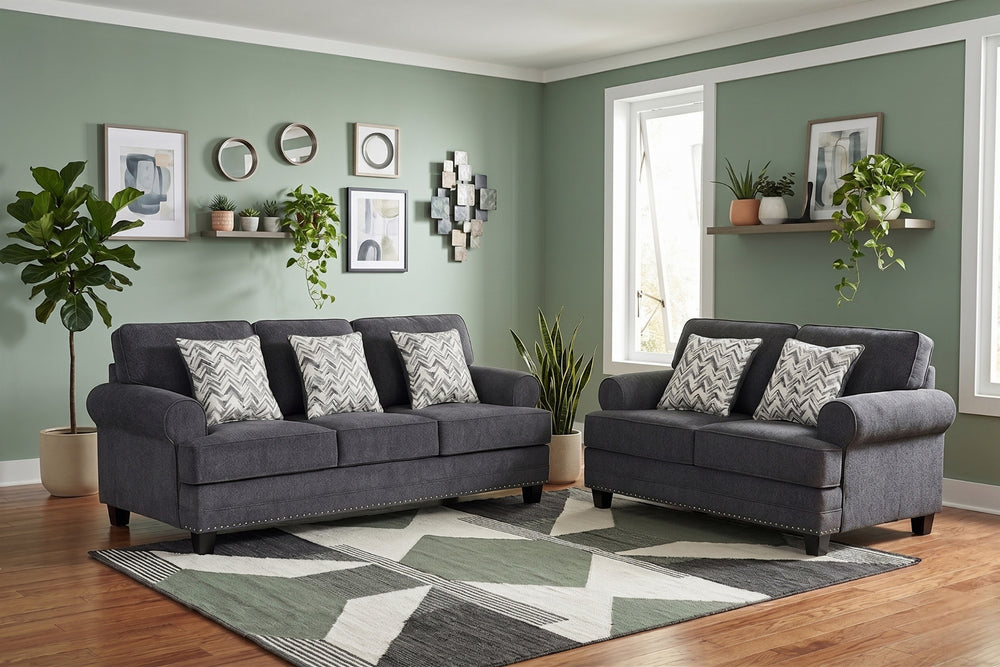 Juego de sala con sofá y loveseat tapizados en tela gris oscuro, brazos redondeados, detalles decorativos de tachuelas metálicas y cojines estampados en patrón geométrico gris y blanco sobre fondo claro.