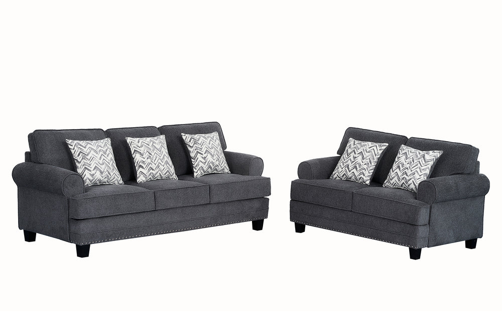 Juego de sala con sofá y loveseat tapizados en tela gris oscuro, brazos redondeados, detalles decorativos de tachuelas metálicas y cojines estampados en patrón geométrico gris y blanco sobre fondo claro.