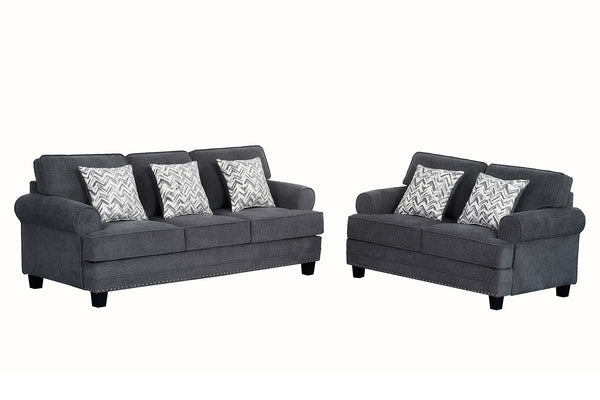 Juego de sala con sofá y loveseat tapizados en tela gris oscuro, brazos redondeados, detalles decorativos de tachuelas metálicas y cojines estampados en patrón geométrico gris y blanco sobre fondo claro.