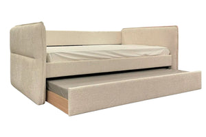 Cama tipo daybed tapizada en tela color beige con respaldo y brazos laterales acolchados. Incluye una cama nido inferior extraíble con mattress, ideal para maximizar espacio y ofrecer una solución versátil para dormir.