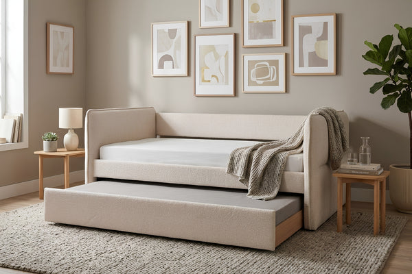 Cama tipo daybed tapizada en tela beige texturizada con cama nido inferior extraíble. Presentada en un dormitorio de estilo contemporáneo con mesas auxiliares de madera, arte mural abstracto y decoración en tonos neutros.